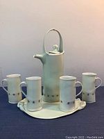 Full view of the tea set with teapot, four mugs, and tray on a navy surface.