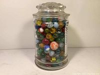 Front and side views of a clear glass jar filled with colorful glass marbles showing a variety of colors and patterns.