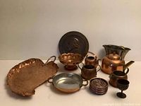 Overview of all metal and copper items showing tray, teapot, coasters, bowls, goblet, pan, planter, and decorative plaque