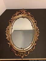 Full view of ornate gold painted oval mirror with intricate scrollwork and floral frame design.