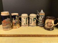 Photo showing all six beer steins in a row on yellow surface.