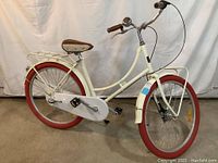 Full left-side view of the off-white ladies bicycle showing frame, wheels, fenders, chain guard, rack and saddle