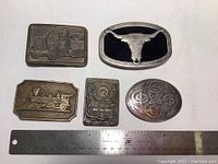 Top view of five vintage belt buckles including two with trains, one with steer skull, one with Celtic design, and solid brass stamped backs