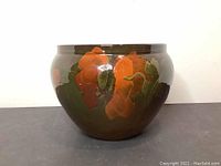 Front view of a rounded brown glazed pottery bowl with bright orange flowers and green leaf patterns painted around the exterior.