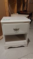 Front view of white painted bedside table showing drawer with metal handle and open shelf below