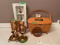 Wide angle photo showing basket, two ceramic cat figures, brass candle holders, and copper cat wind chime on floor near wall