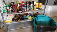Shelving unit holding multiple bottles of car care products, cloths, mitts, and brushes organized on two shelves.