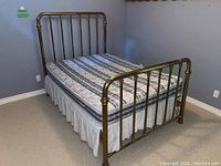 Side angle view of the vintage brass bed frame assembled with mattress and bedskirt showing headboard and footboard design and condition.