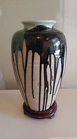 Front view of the hand painted pottery vase on wooden stand, showing abstract black drip design over green and beige background with glossy finish.