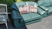 Green leather loveseat with two armrests and three decorative throw pillows with geometric patterns arranged on the seat cushions.