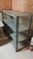 Full view of galvanized metal shelf with four shelves in basement corner next to table, showing overall condition and structure.