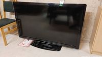 Front view of the Philips 55 inch HD LCD television showing the screen, stand, remote, and manual on the floor beside it.