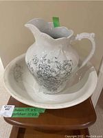 Front view of vintage ceramic pitcher and basin set with floral and scroll motifs on a wooden surface.