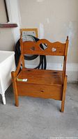 Front view of small wooden bench seat showing hinged storage seat and heart-shaped cutouts on backrest.