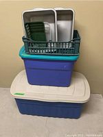 Storage bins piled with a green vented basket containing gray trays and basins on top of the bins.