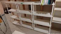 Three white plastic shelf units attached to wall; shows three units side by side with plastic hangers on top shelf