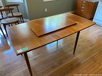 Overall view of teak dining table partially extended with one leaf on top