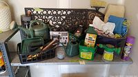 Assorted gardening items on a shelf including watering cans, garden tools in black caddy, fertilizer containers, and outdoor mat.