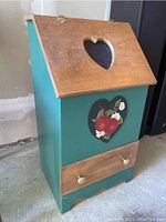 Front view of the wooden vegetable storage box showing teal painted body, hinged lid with heart cutout and hand painted tomato decoration on front.