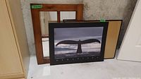 Photo of three items together: wood framed windowpane mirror at the back, photographic poster on board in front, and empty wood frame with glass leaning against the wall.