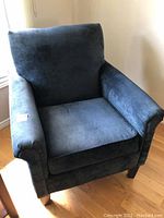 Front view of the navy blue upholstered armchair showing cushioned seat and backrest with wooden legs.
