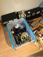 Photo of cassette tape cases, a plastic tote with cables and cords, and part of the floor