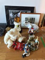 Photo showing Wizard of Oz print, Trisha Romance print in frame, Royal Dux white ceramic elephant with broken tusk, soft white teddy bear, Santa and other holiday figurines, Noah candle circle with multiple animal figures, small brass clock and globe music box.