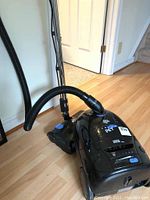 Black Dirt Devil Jaguar Pet vacuum canister with hose and wheels on hardwood floor