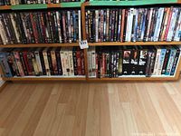 Wooden shelves with multiple rows of DVDs and VHS tapes including movies and TV shows, showing a wide range of titles.