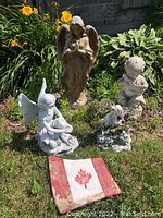 All garden decor items arranged together including large angel, three resin figures, and painted stone flag