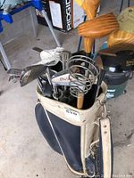 Full view of golf clubs inside vintage-style golf bag showing wooden drivers, iron clubs, and a metal putter