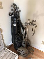 Black golf bag with 16 golf clubs inside surrounded by a metal golf push caddy and other accessories