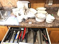 Overview of white CorningWare plates, bowls, casserole, platter, and egg cups arranged on countertop near sink