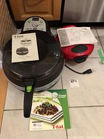 T-Fal ActiFry air fryer alongside Hamilton Beach quesadilla maker on floor with their manuals
