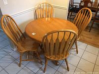 Full view of round honey oak table with four matching chairs arranged around it, showing shape, style and condition.