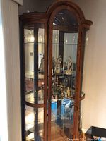 Full view of the oak curio cabinet showing the bent glass side lights, arched top, and glass shelves with display items inside.
