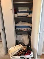 Photo showing folded assorted linens including towels, blankets, white cloths, hangers and laundry hampers in a white shelving unit.