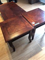 Photo showing two wooden side tables with square tops and curved legs, placed next to a wooden coffee table.