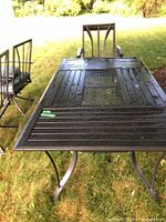 Photo of rectangular black metal outdoor table with slatted and perforated top surface taken outside on grass