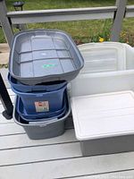 Photo of a stack of five plastic storage totes in various colors (grey, blue, white) showing their shapes and relative sizes.