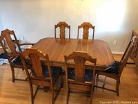 Full view of walnut dining table with 6 chairs arranged around it, showing the design and upholstery of chairs.