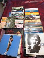 Photo showing collection of vinyl records laid out on a red surface, covers partially visible including various artists and albums