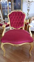 Front view of the ornate armchair showing red velvet upholstery on the tufted backrest and seat with carved wood frame and curved legs.