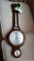 Full view of wooden barometer with thermometer and hygrometer mounted on it, showing the entire piece with brass-framed circular dials and rounded glass.