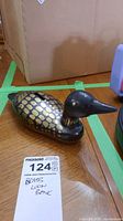 Brass loon bank angled to show the side, displaying brass black and gold painted scales with felt bottom under it.