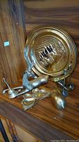 Photo showing the brass deer figurine, three brass candle holders, a small heart-shaped brass dish, and a round brass embossed plaque with horse and plow scene.