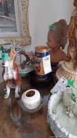 Photo showing the bust, ceramic dog figurine, candle in a blue container, and other small decorative items on the table