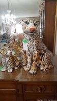 Three ceramic leopard figurines on wooden surface in front of mirror showing chandelier reflection