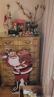 Full view of a dresser with Christmas decorations including faux white tree with lights and ornaments, hand-painted large Santa figure attached to dresser, nutcracker figures, and other decorations on top of dresser.
