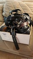 Box filled with a variety of black and brown leather belts, showing different buckle styles and belt widths.